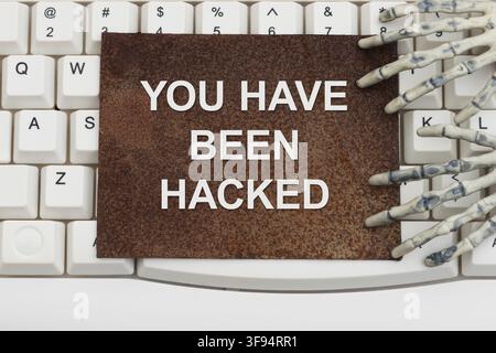 Sie wurden gehackt - Text auf rostigem Schild mit Skeletthänden auf einer weißen Computertastatur für Cybersicherheit Stockfoto