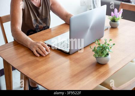 Eine Person sitzt an einem Holztisch und benutzt eine Computermaus neben einem Laptop. Remote-Arbeitslebensstil, Home-Office-Freelance, moderner Arbeitsplatz. Stockfoto