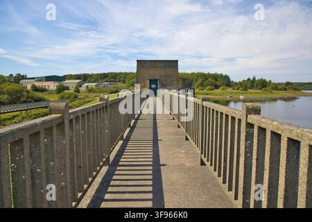 Erhöhter Gehweg oben auf dem Llyn Cefni-Staudamm, der zum zentralen Kontrollturm in Anglesey, Wales, führt. Stockfoto