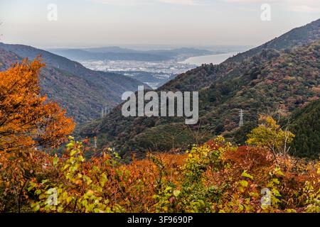 Ein herbstfarbener Wald umrahmt eine Aussicht von den Hakone-Bergen zur Küste, in der Ferne möglicherweise Odawara und die Sagami-Bucht. Präfektur Kanagawa, Japan. Stockfoto