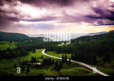 Blick auf ein stürmisches Bergtal vom Cumbres & Toltec Zug. Eine regennasse Autobahn windet sich durch die düstere, bewaldete Landschaft. Stockfoto