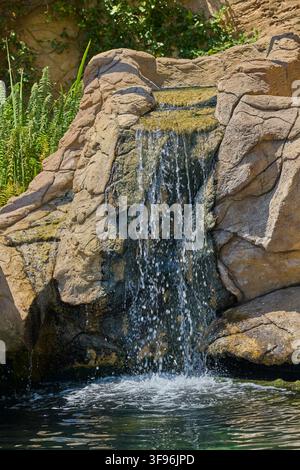 Kleiner Wasserfall fließt über natürliche Felsen in einen klaren Teich. Stockfoto