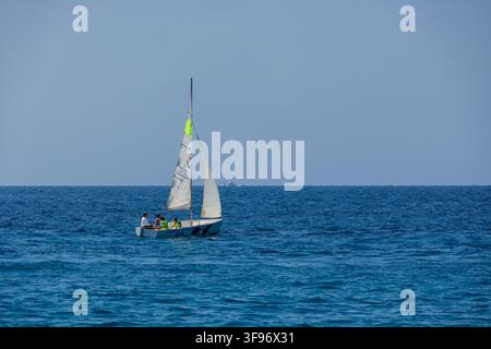Calp, Spanien - 11. Juli 2027: Blick auf ein kleines Segelboot mit Menschen an Bord, das auf dem ruhigen blauen Mittelmeer unter einem klaren Himmel segelt. Stockfoto