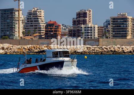 Calp, Spanien - 11. Juli 2027: Blick auf ein Motorboot, das auf dem Mittelmeer kreuzt, mit der modernen Skyline der Stadt im Hintergrund. Stockfoto