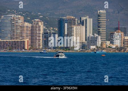 Calp, Spanien - 11. Juli 2027: Blick auf die Küsten skyline mit modernen Hochhäusern, einem Motorboot, das auf dem blauen Mittelmeer kreuzt, und klarem Stockfoto