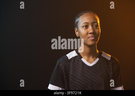 Afroamerikanische Frau posiert im Studio, trägt schwarzen Jersey mit weißem Rand, geflochtene Haare, Kopierraum Stockfoto