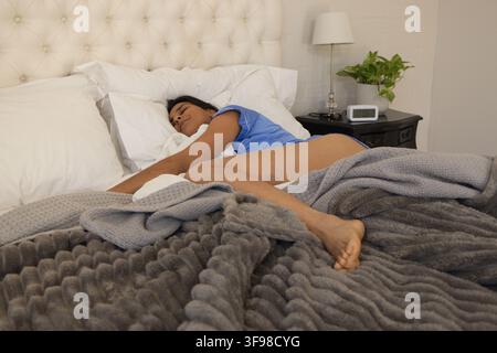 Indische Frau schläft auf einem großen Bett im Schlafzimmer, trägt hellblaue Schlafkleidung mit Kissen und Lampe Stockfoto