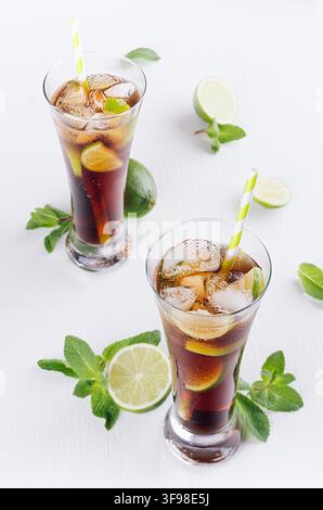 Sommerfrische kohlensäurehaltige Cola mit Eis in zwei Gläsern mit Minze und Limette auf weißem Holzbrett, Blick von oben. Stockfoto