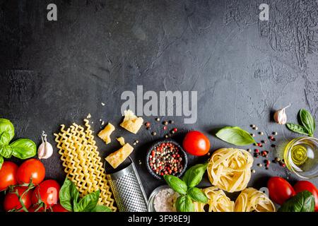 Hintergrund Pasta. Verschiedene Arten von trockener Pasta mit Gemüse und Kräutern auf schwarzem Hintergrund. Freier Platz für Text. Draufsicht Stockfoto