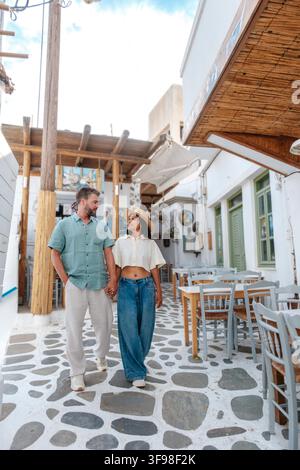 Ein Paar geht Hand in Hand durch die charmanten Gassen von Naxos, Griechenland, umgeben von weiß getünchten Gebäuden und rustikalen Cafés, und genießt einen friedlichen Tag unter dem blauen Himmel. Stockfoto