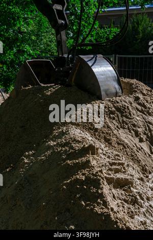 Nahaufnahme eines Baggerlöffels, der in einem Sandhaufen auf einer Baustelle ruht. Generische Erdbewegungs- und Ausgrabungsszene. Stockfoto
