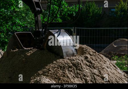 Nahaufnahme eines Baggerlöffels, der in einem Sandhaufen auf einer Baustelle ruht. Generische Erdbewegungs- und Ausgrabungsszene. Stockfoto