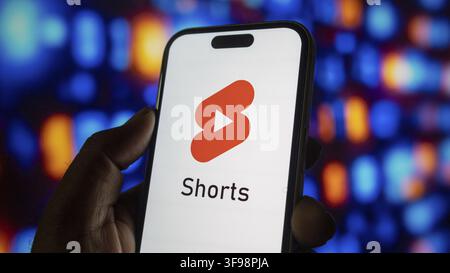 Hand, die ein Smartphone mit roter App-Schaltfläche für Shorts zeigt, helles Interface-Design, unscharfe bunte Lichtkreise im Hintergrund, kurze Form vi Stockfoto
