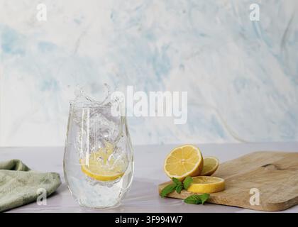 Zitronenscheiben, die in ein Glas Wasser spritzen, umgeben von einer frischen und luftigen Atmosphäre Stockfoto