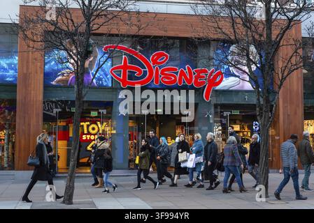 Menschen, die an der farbenfrohen Schaufensterfront des Disney Toy Store in der Oxford Street in London an einem trockenen Winterabend vorbeigehen Stockfoto
