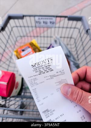 ADDISSON, TX, USA - 26. JULI 2026: Eine Person hält einen Kassenzettel von Sprouts Farmers Market über einen Einkaufswagen voller Lebensmittel. Sprouts ist bekannt für Stockfoto