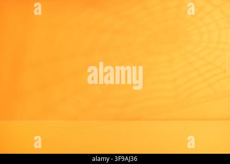 Minimaler orangefarbener Halloween-Hintergrund mit dezentem Spinnennetz-Schatten und leerer Tischfläche für Produkt-Mockup-Banner oder Party-Display Stockfoto