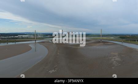 Luftbild der Mersey Gateway Bridge, die bei Ebbe die River Mersey überspannt, mit industriellen Kühltürmen in der Ferne unter einem bewölkten Himmel in Ru Stockfoto