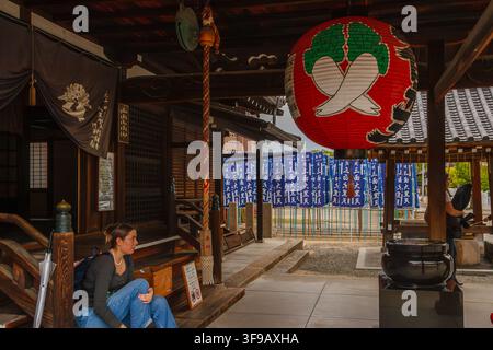 Eine junge Touristin sitzt in der Nähe des Eingangs des Daikokudo-Pavillons unter einer riesigen roten Papierlaterne im Shitennoji-Tempel in Osaka, Japan. Stockfoto