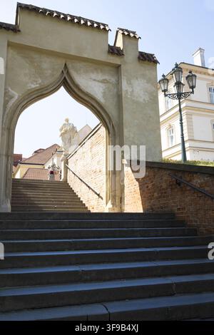 Brno, Tschechische Republik. 11. August 2026. Eine Steintreppe führt durch ein gewölbtes Tor nach oben. Eine Statue steht an der Spitze der Treppe, und ein dekorativ Stockfoto