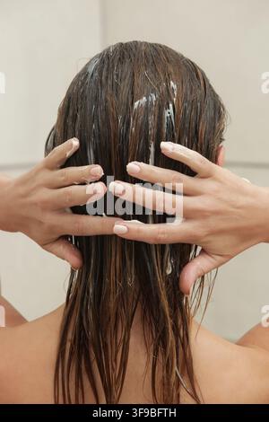 Nahaufnahme einer Frau, die Haarspülung aufträgt für weiches, glattes und gesundes Haar Stockfoto