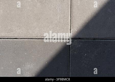 Eine Hochwinkel-Makrofotografie von quadratischen Betonpflasterplatten auf einem Fußgängerweg im Freien, die einen scharfen diagonalen Schatten zeigen. Stockfoto