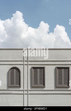 Eine Nahaufnahme einer weißen Betongebäudefassade mit horizontalen und vertikalen Formlinien, drei dunkelbraunen verschlossenen Fenstern Stockfoto