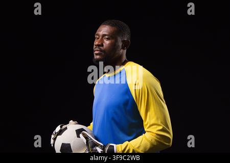 Mittelalter Mann posiert im Studio, trägt gepolsterte TorwartHandschuhe und Trikot, hält Fußball Stockfoto