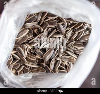 Nahaufnahme von Sonnenblumenkernen in einem durchsichtigen Plastikbeutel, die ihre unterschiedlichen Formen und Texturen vor einem dunklen Hintergrund zur Schau stellen Stockfoto
