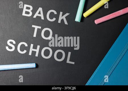 Oberblick-Komposition des Textes "Zurück zur Schule" gedruckt auf einer schwarzen Tafel mit bunten Kreidestücken und einem blauen Notizbuchrand. Hochwertiges Foto Stockfoto