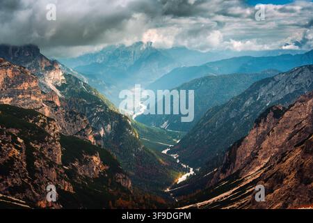 Dramatische alpine Landschaft mit felsigem Berggipfel, gewundenem Fluss und Sonnenlicht, das durch den bewölkten Himmel in den Dolomiten, Italien, scheint Stockfoto