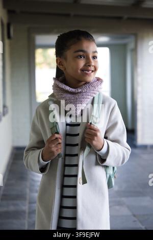 Afroamerikanische Teenagerin steht im Flur und hält einen mintgrünen Rucksack und einen pinken Schal Stockfoto