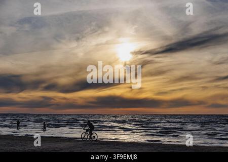 Silhouette eines Radfahrers, der auf einem sandigen Strand in Majori, Jurmala, Lettland während des Sonnenuntergangs Fahrrad fährt Stockfoto