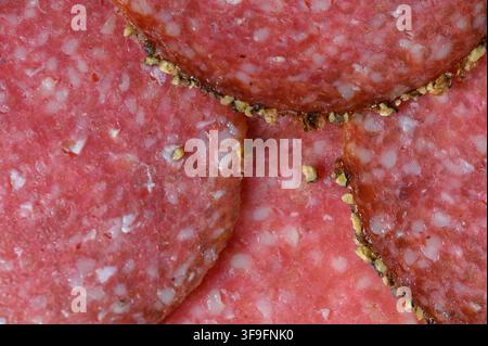 Eine detaillierte Makroaufnahme, die sich überlappende dünne Scheiben von gereifter Salami-Wurst zeigt, wobei die feine Textur von fein gehacktem Fleisch, weißen Fettpunkten und Stockfoto