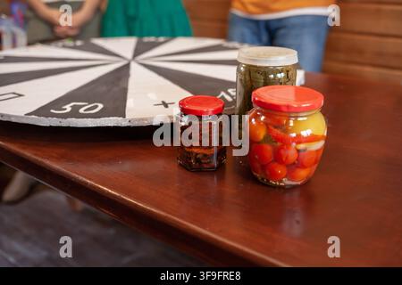 Gläser mit eingelegten Gemüse und Früchten auf einem Holztisch neben einem sich drehenden Spielrad in einer lässigen Indooreinrichtung Stockfoto