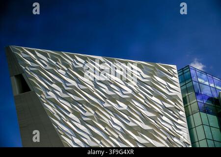 Die kantige Aluminiumfassade des Titanic Belfast erzeugt dramatische geometrische Muster vor einem blauen Himmel im Titanic Quarter. Stockfoto