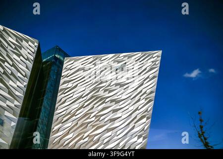 Die kantige Aluminiumfassade des Titanic Belfast erzeugt dramatische geometrische Muster vor einem blauen Himmel im Titanic Quarter. Stockfoto