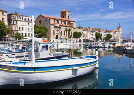 Ein weißes und blaues Fischerboot, das im alten Hafen von La Ciotat vor Anker liegt, mit Kirche und historischer Stadt im Hintergrund, Frankreich. Stockfoto