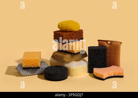 Verschiedene Küchen- und Reinigungsschwämme gestapelt und auf einem soliden hellgelben Hintergrund mit harten Schatten angeordnet Stockfoto