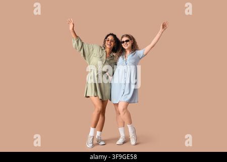 Zwei glückliche junge Frauen in lässigen Kleidern und Sonnenbrillen mit erhobenen Armen, die Freundschaft und Sommer mode feiern Stockfoto