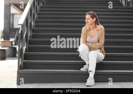 Junge Frau mit Magenschmerzen, die auf Außentreppen sitzt, Gesundheit und Unbehagen Stockfoto