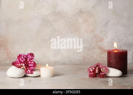 Spa-Umgebung mit brennenden Kerzen, Orchideenblüten und weißen Steinen für Entspannung und Wohlbefinden Stockfoto