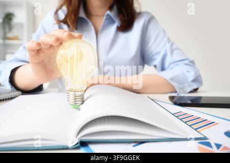 Geschäftsfrau hält eine Glühbirne über ein offenes Notizbuch neue Ideen Innovation und kreative Problemlösung in der Geschäftsfrau Stockfoto