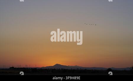 Luftbild eines Sonnenuntergangs über einer Landschaft mit fernen Windrädern und Bergen, auf denen Vögel am Himmel über Zypern fliegen, Zypern. Stockfoto