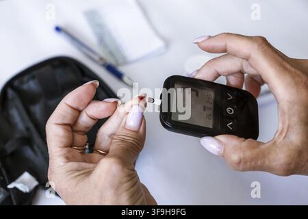 Nahaufnahme von weiblichen Händen, die einen Teststreifen in ein Blutzuckermessgerät einlegen, vor dem Diabetes-Test. Heimüberwachung, Endokrinologie, Gesundheitstechnologie Stockfoto