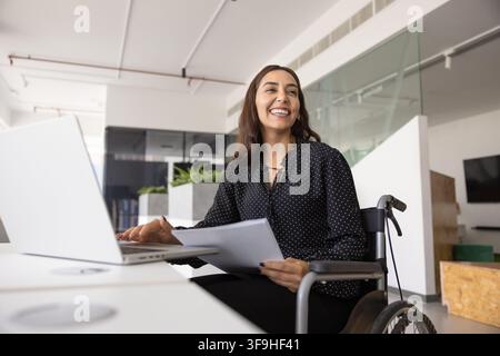Lächelnde Geschäftsfrau im Rollstuhl, die an einem Laptop arbeitet Stockfoto