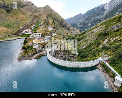 Luftaufnahme der Diga e Lago di Malciaussia mit ihrer gebogenen Staumauer, den umliegenden grünen Berghängen und kleinen Gebäuden, die sich in den Hügel schmiegen Stockfoto