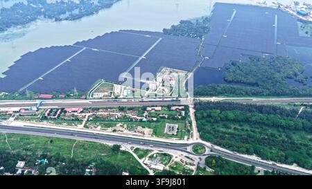 Luftaufnahme des Sirajganj 68 MW Solarparks mit umfangreichen Solarpanel-Arrays, die auf Wasser installiert sind, angrenzend an eine Eisenbahnstrecke und eine Autobahn in Sirajga Stockfoto
