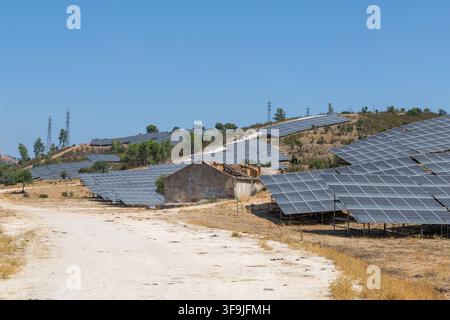 Reihen von Photovoltaik-Panelen erstrecken sich über eine trockene, hügelige Landschaft unter einem hellen, wolkenlosen Himmel und zeigen die Infrastruktur für erneuerbare Energien Stockfoto