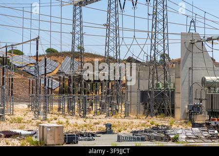 Ein weitläufiges Solarenergie-Feld ist in eine komplexe elektrische Trafostation mit Hochspannungsleitungen und großen Transformatoren integriert Stockfoto
